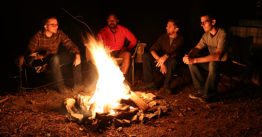 Men talking together around a glowing campfire